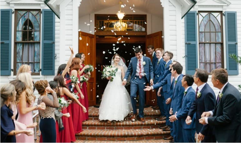 Hunter and Erika exiting a white chapel through tossed petals on their wedding day