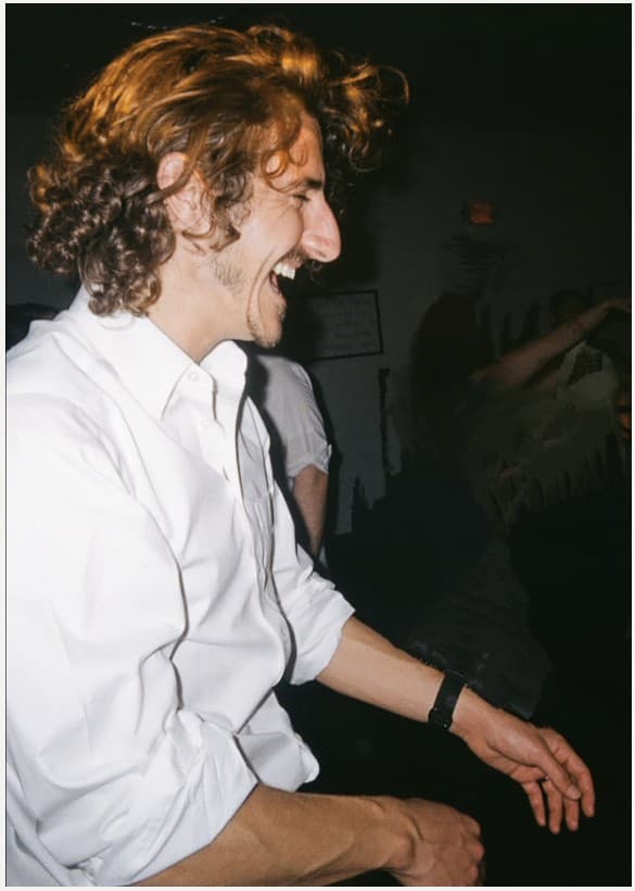 Film-style flash photo of Hunter laughing in a white button-down