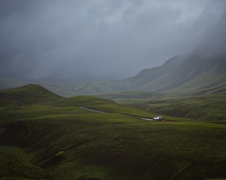 Moody storm clouds over a green valley with a lone white truck on a dirt road