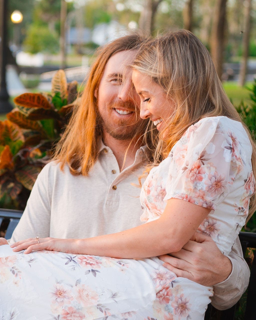 Engaged couple laughing on park bench golden hour light