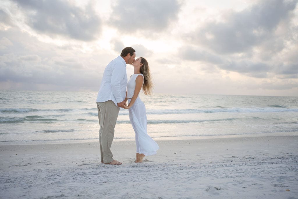 Couple kissing on empty white sand beach cloudy sunset