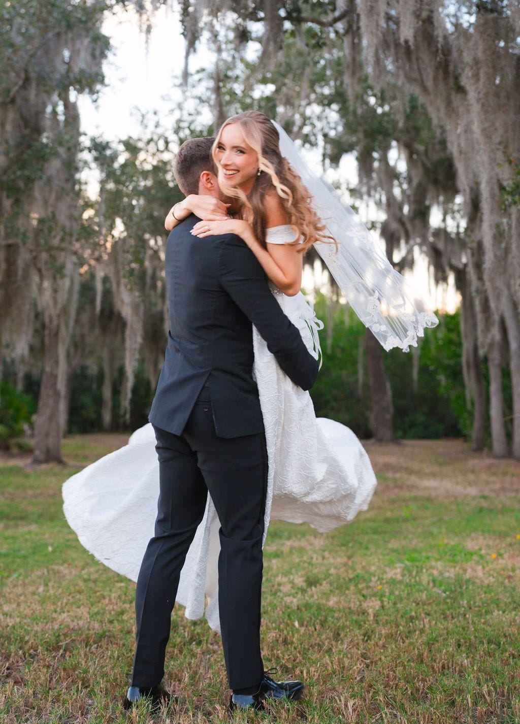 Groom lifting bride under Spanish moss oaks sunset