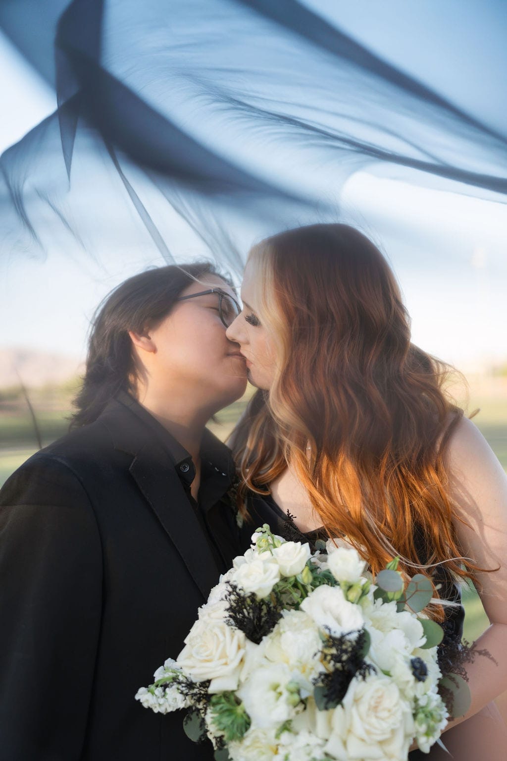 Newlyweds kissing under flowing black veil golden hour