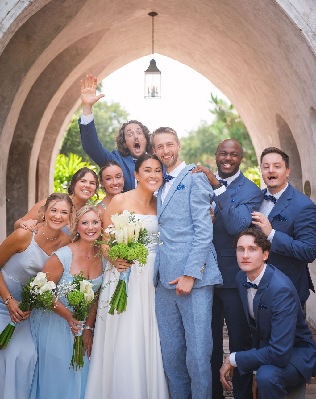 Wedding party under stone arch blue suits light blue dresses