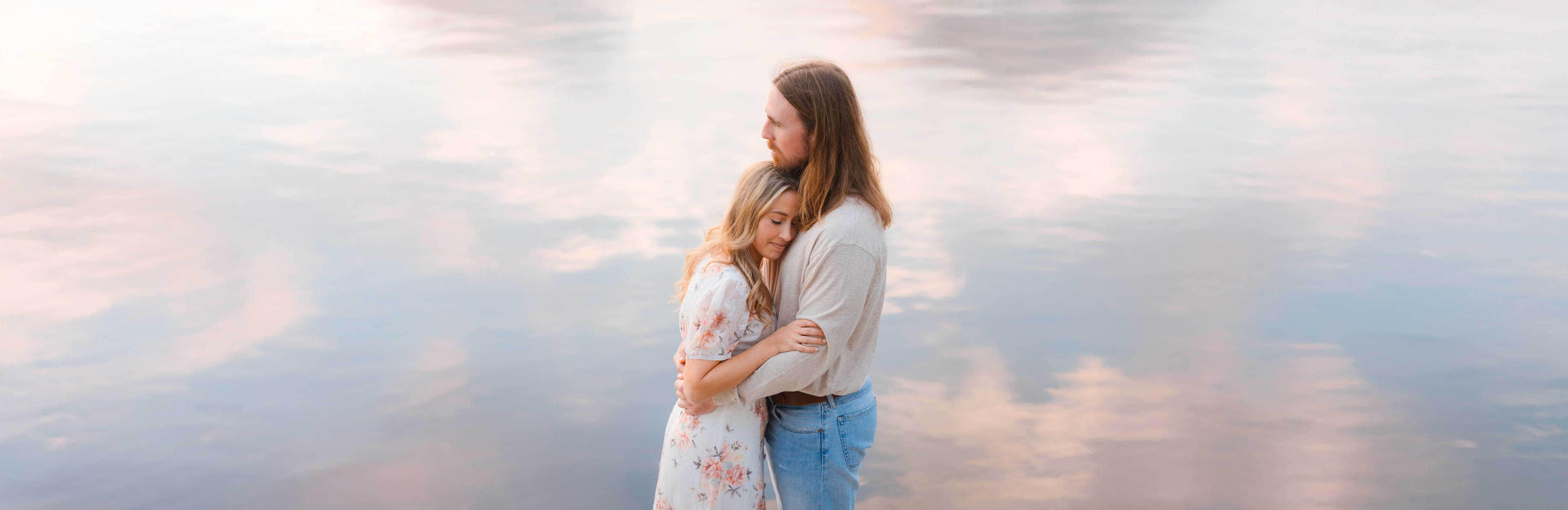 Couple embrace mirrored sunset water pastel sky