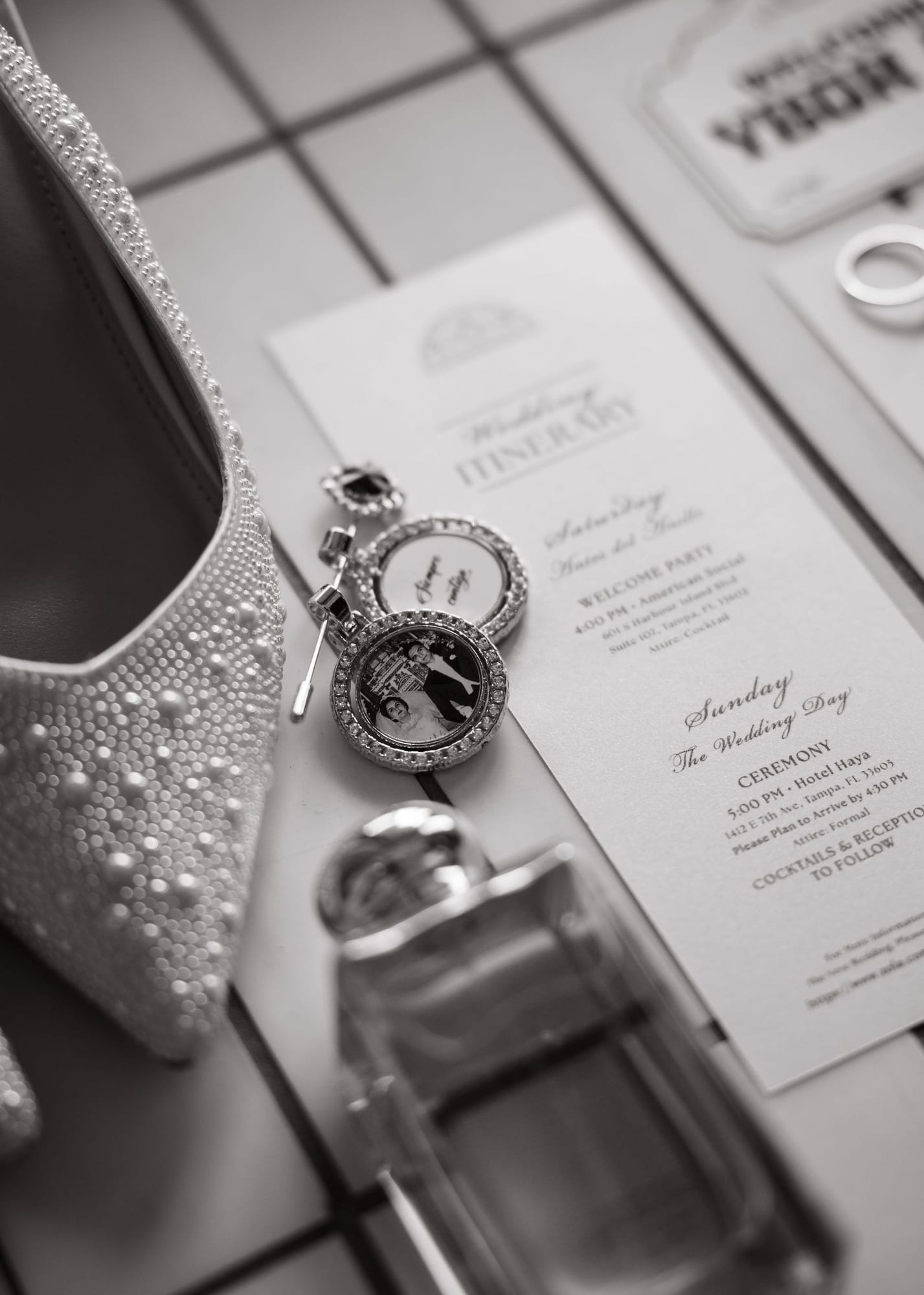 Black and white flat lay of wedding shoes, perfume and invitation