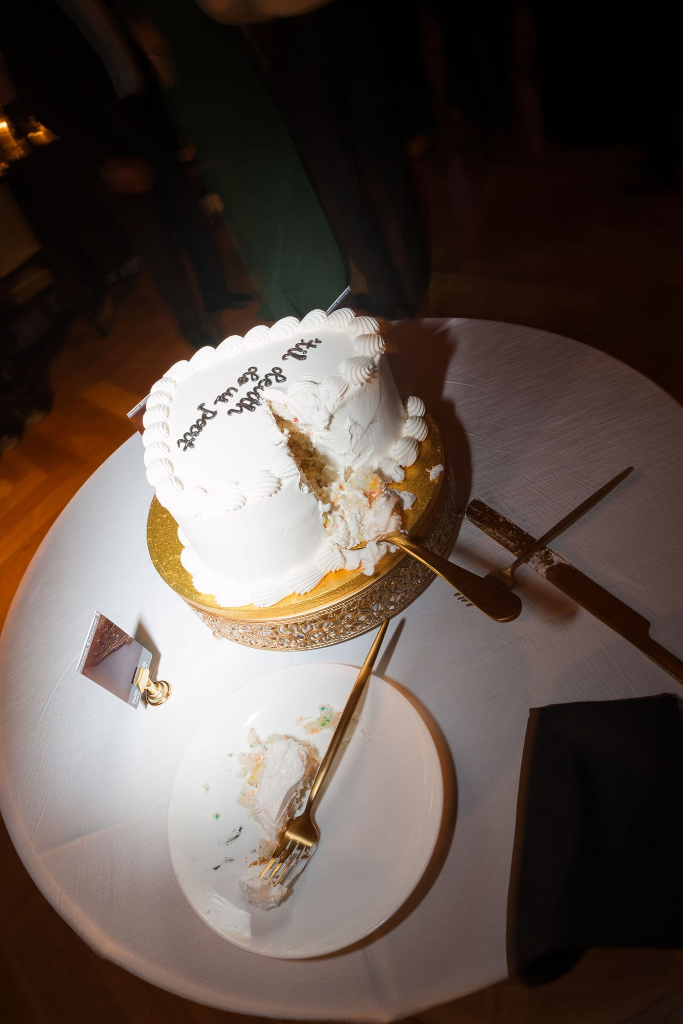 Wedding cake on a gold stand at a reception with warm lighting