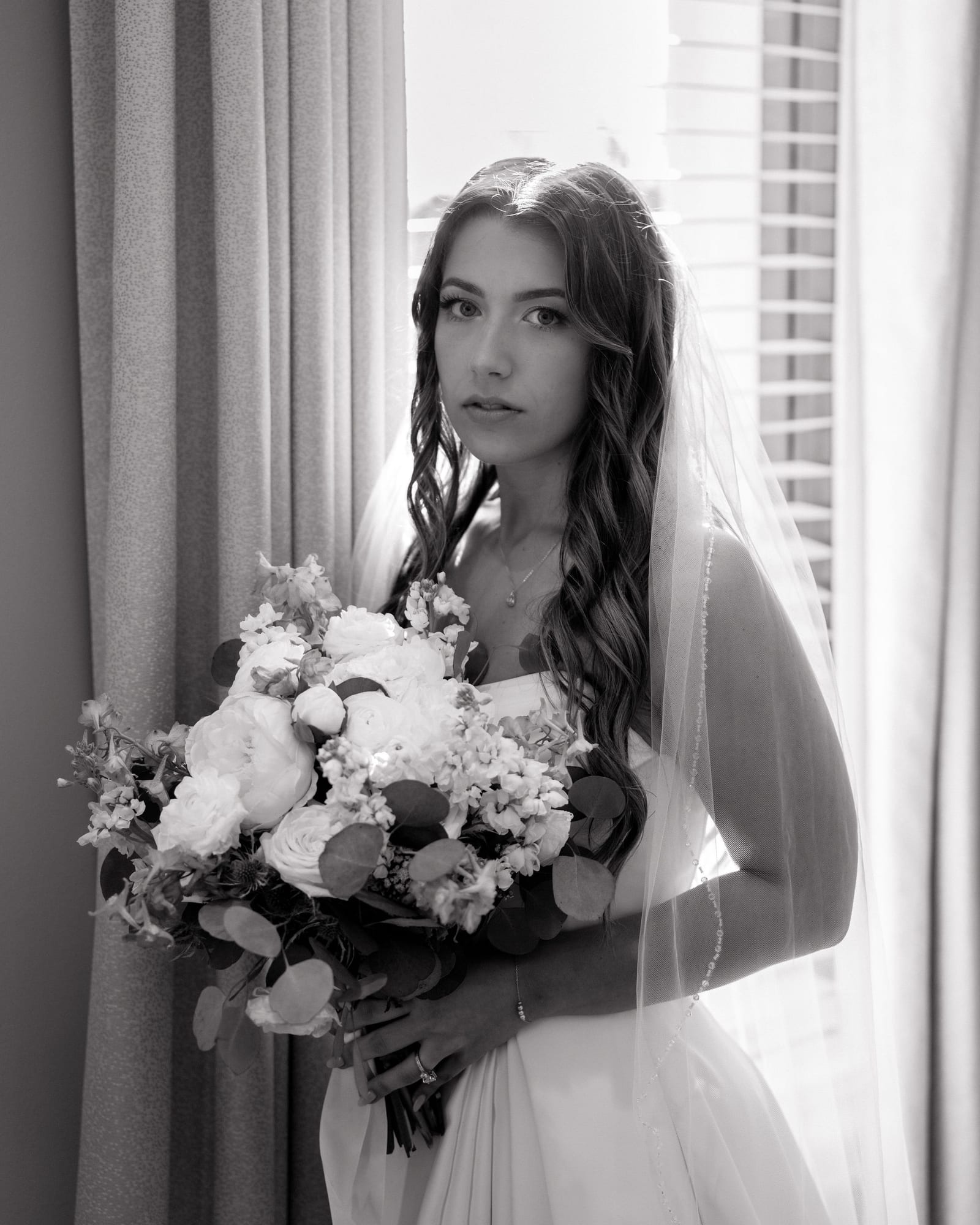 Bride in window light holding her white and blue bouquet