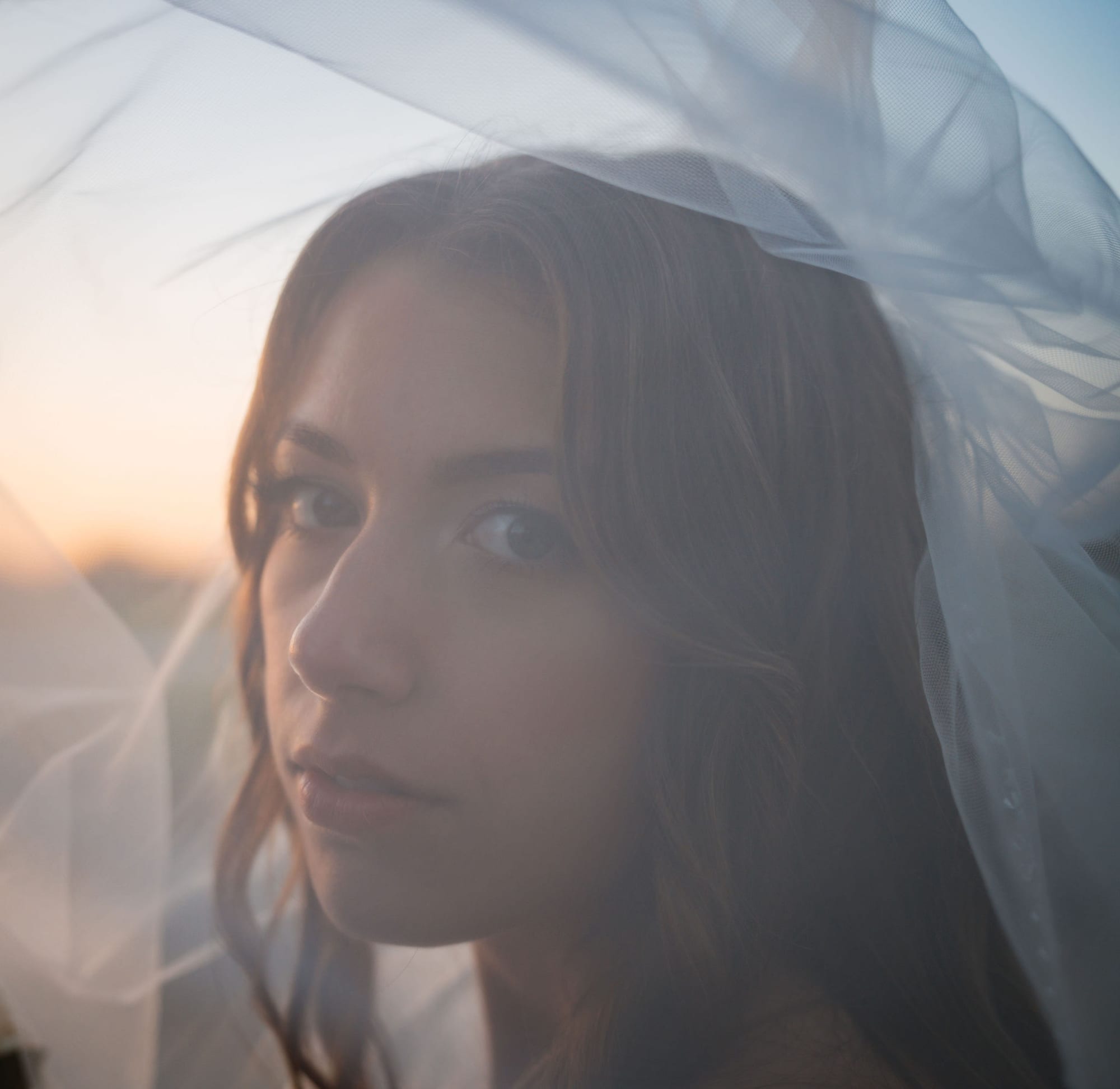 Bride under her veil in warm golden hour light on the golf course