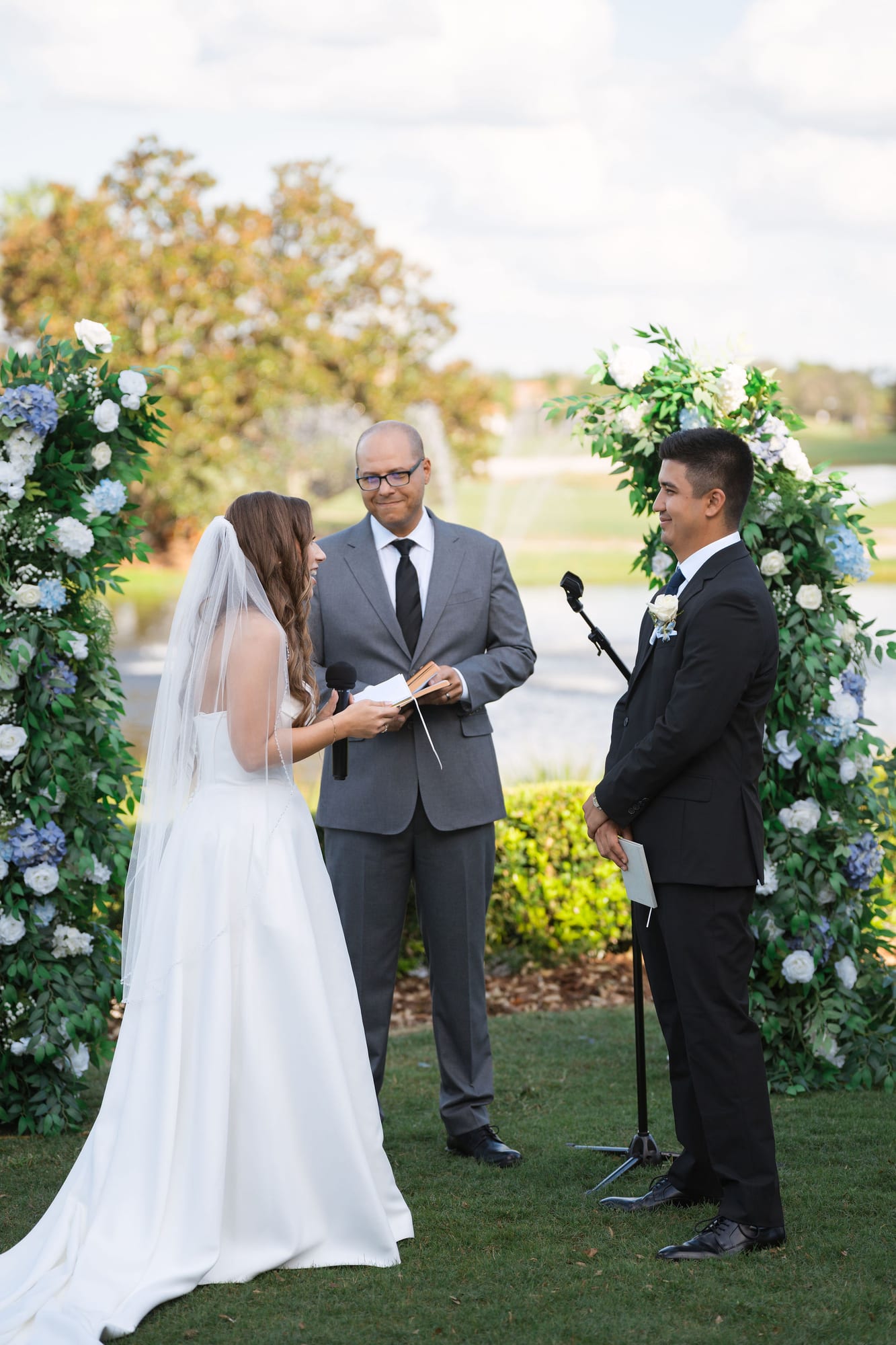 Bride and groom at the floral ceremony arch beside the lake