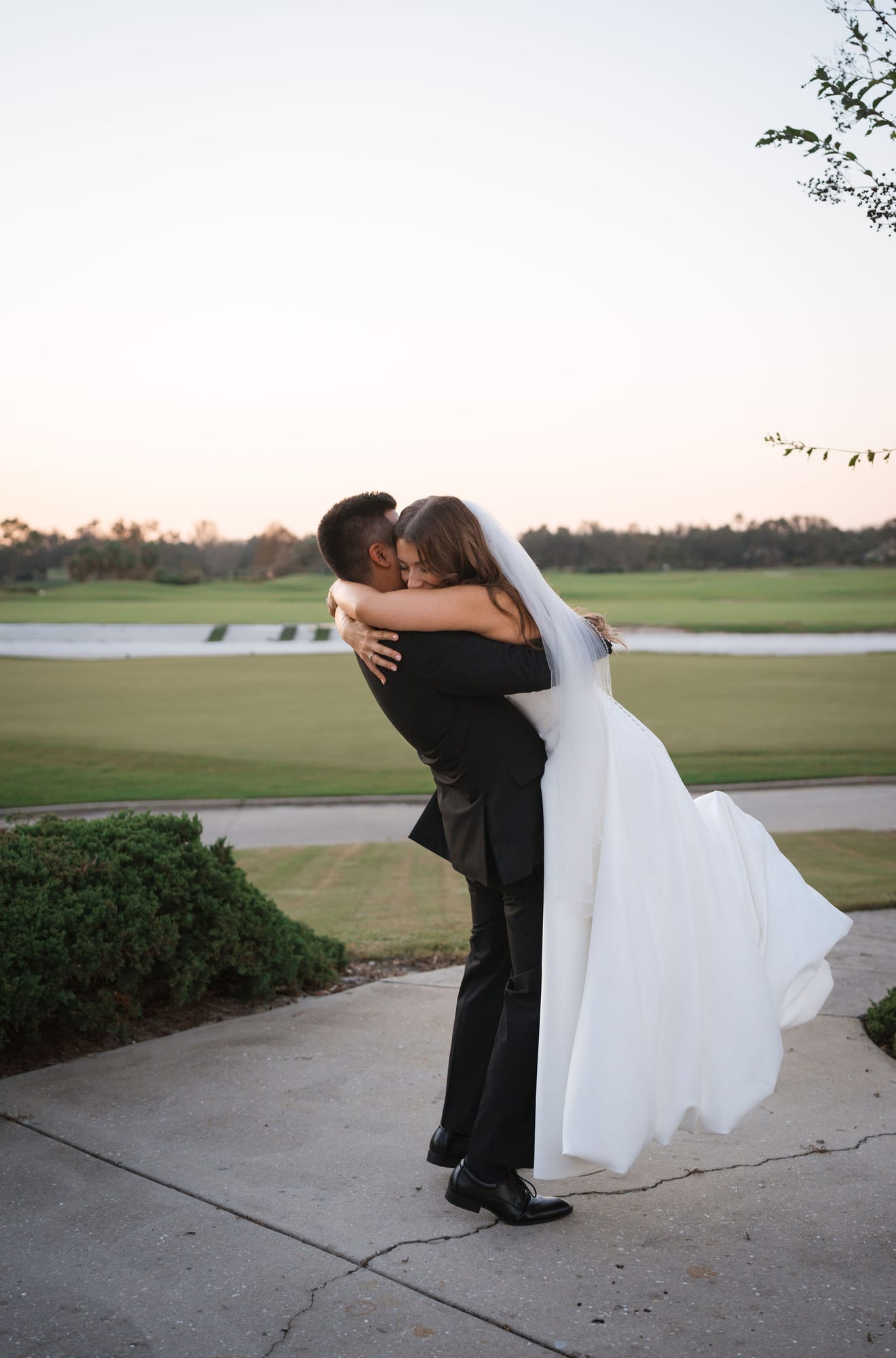 Groom lifting his bride at sunset on the golf course