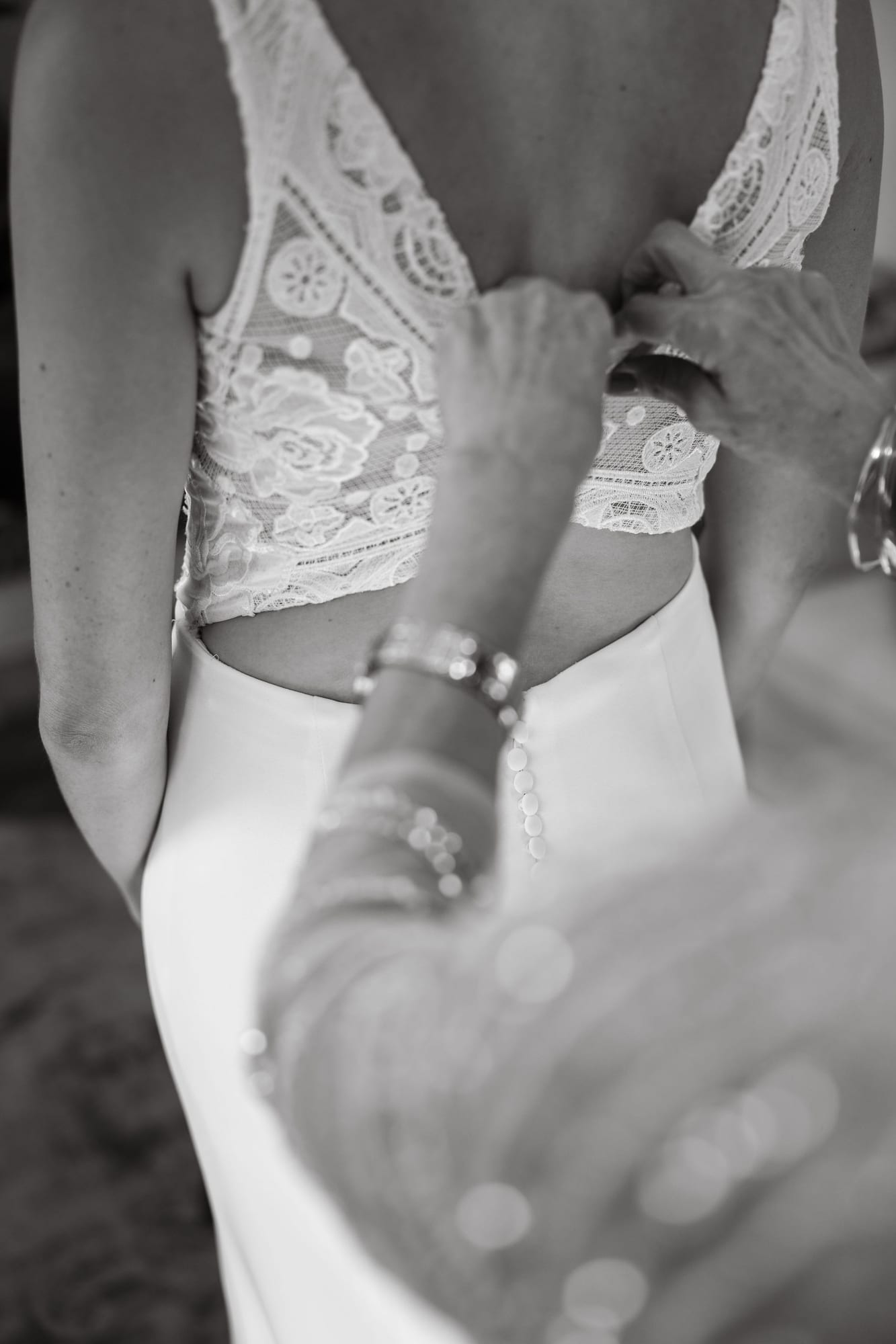 Black and white detail of the wedding dress being buttoned up the back