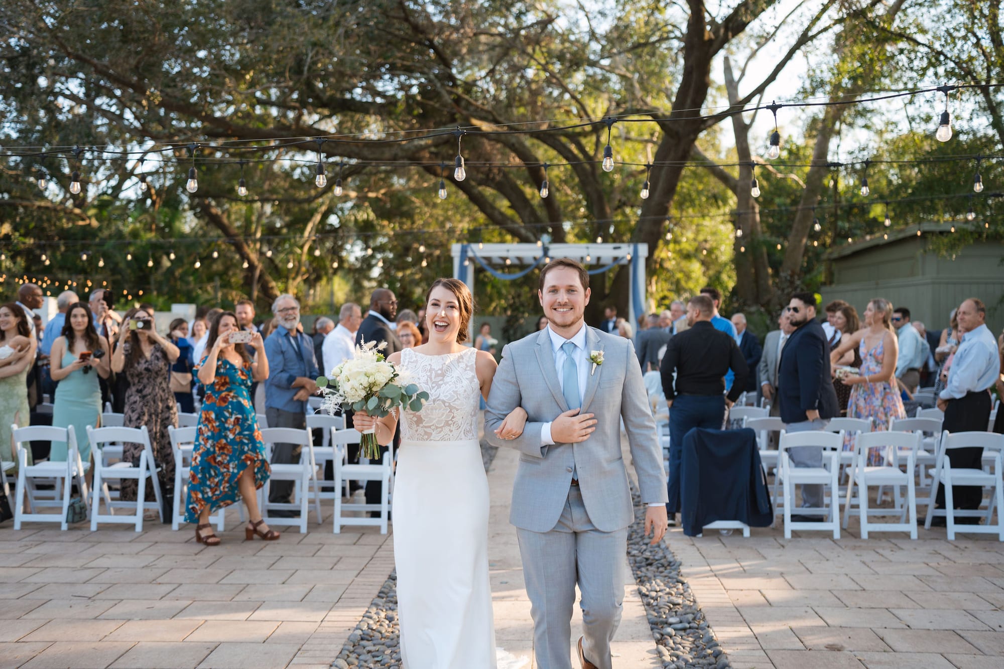 Newlyweds walking back up the aisle surrounded by guests under the live oaks