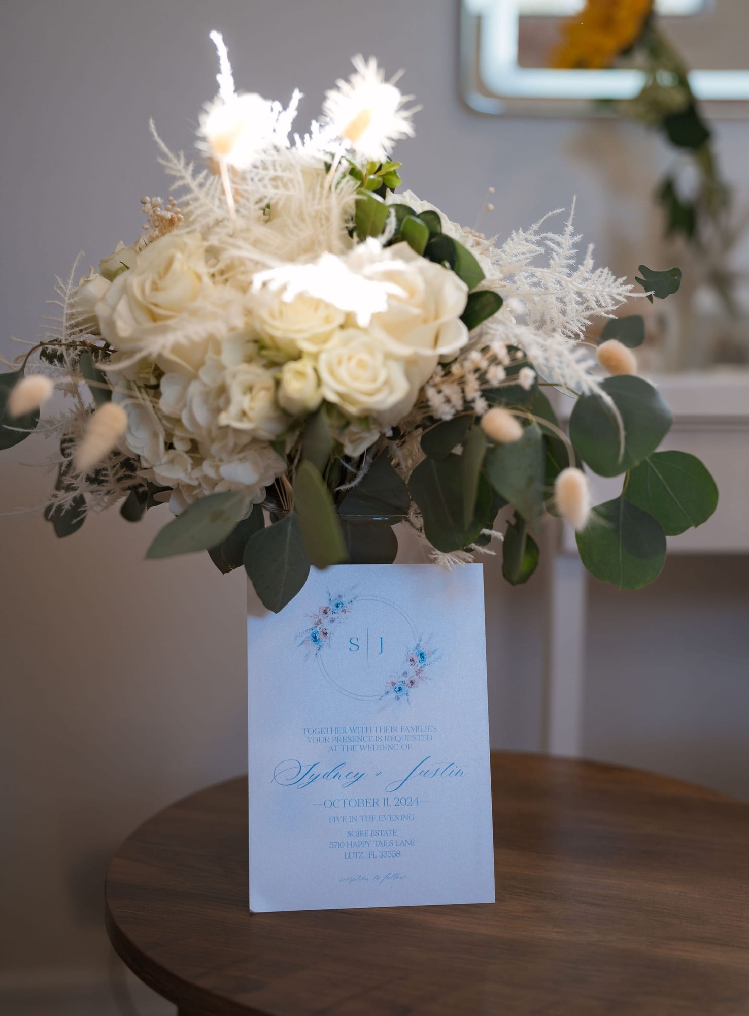 Wedding invitation suite beside a white rose bouquet with dusty blue accents