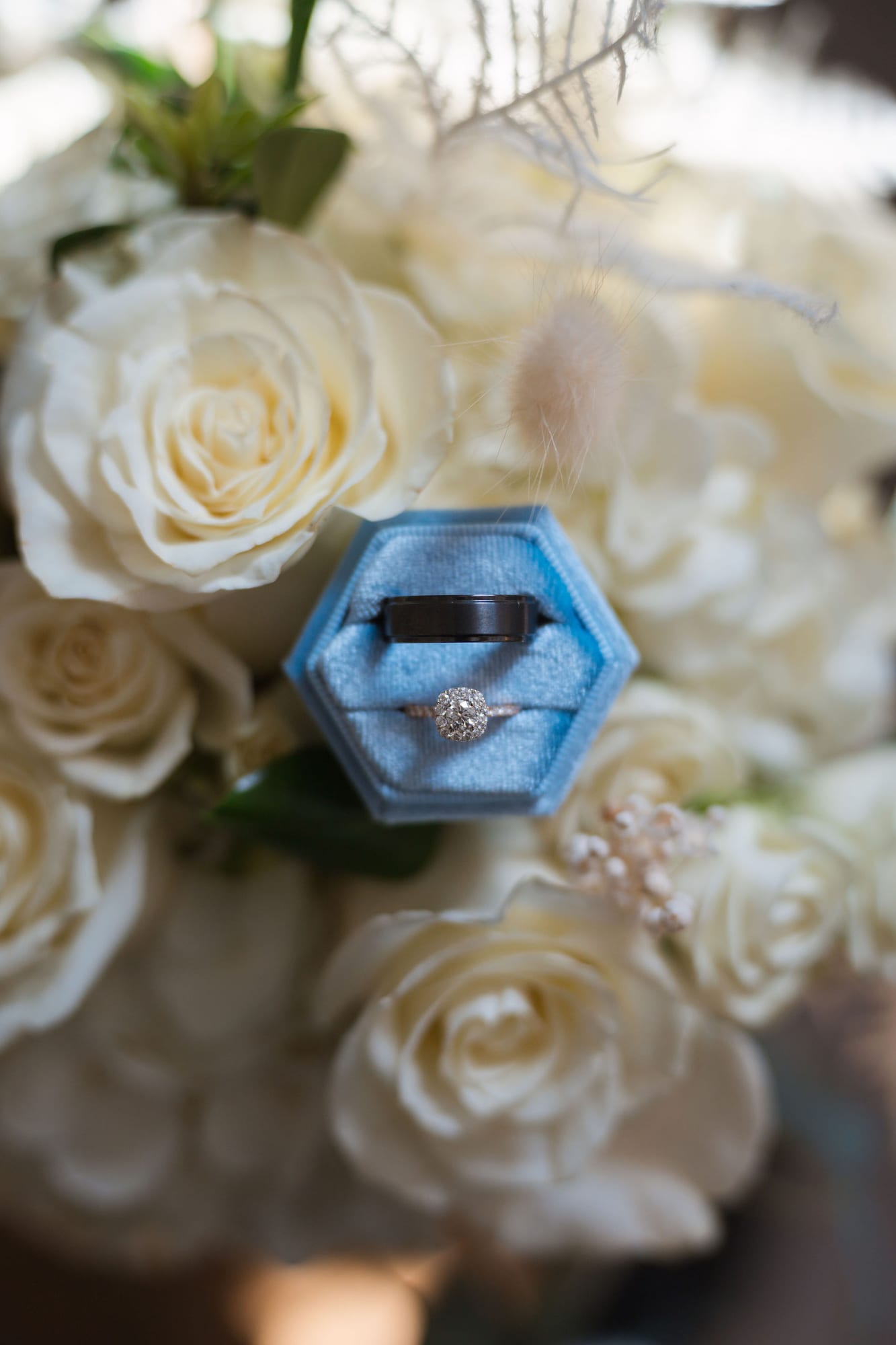 Wedding rings in a dusty blue ring box resting on white roses