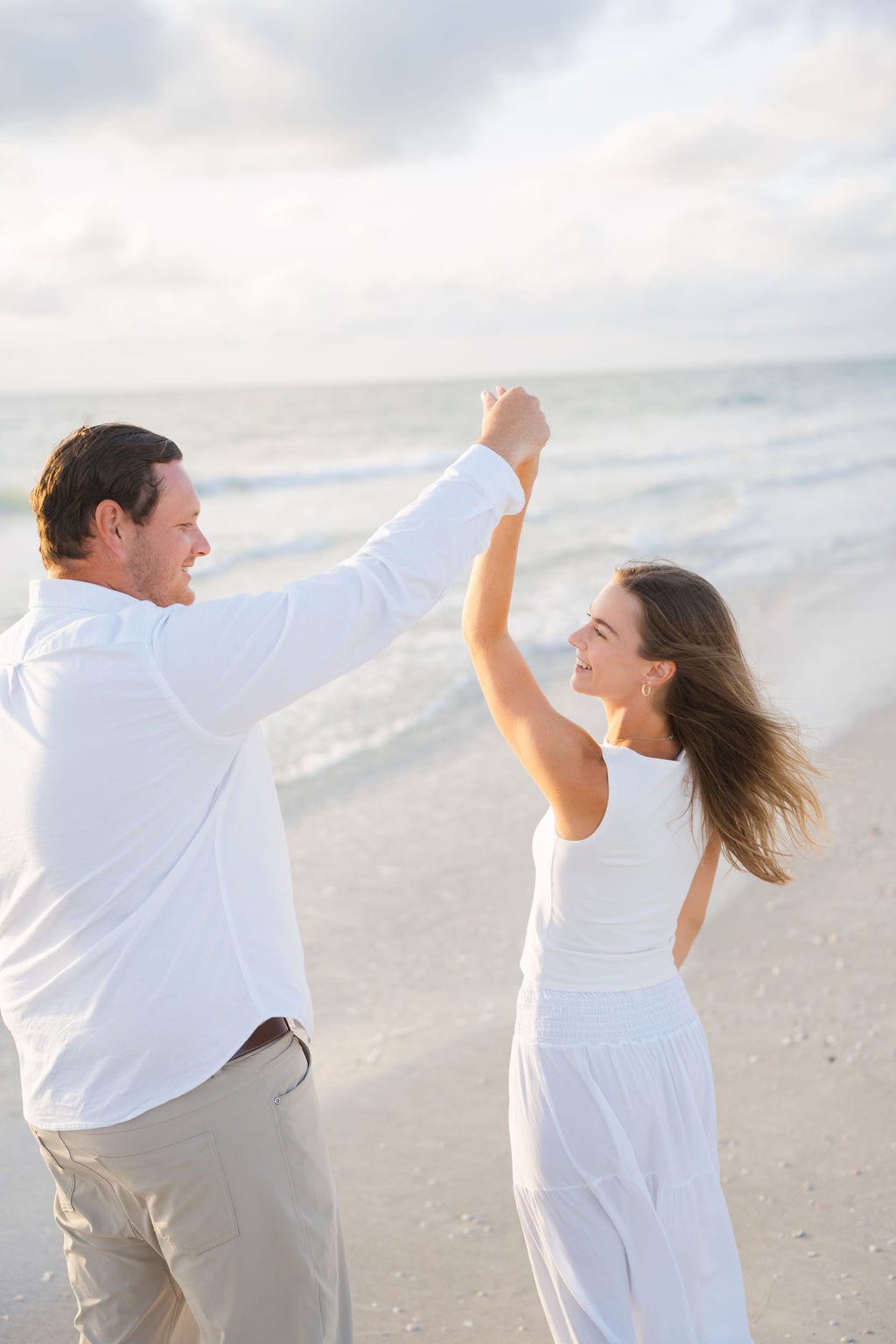 Fiance twirling partner in a white dress on a Gulf coast beach near Clearwater