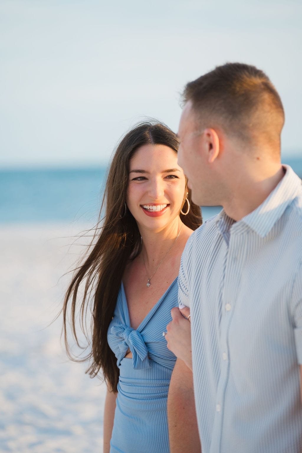 Bride to be laughing with her fiance in a blue dress during a golden hour beach engagement session