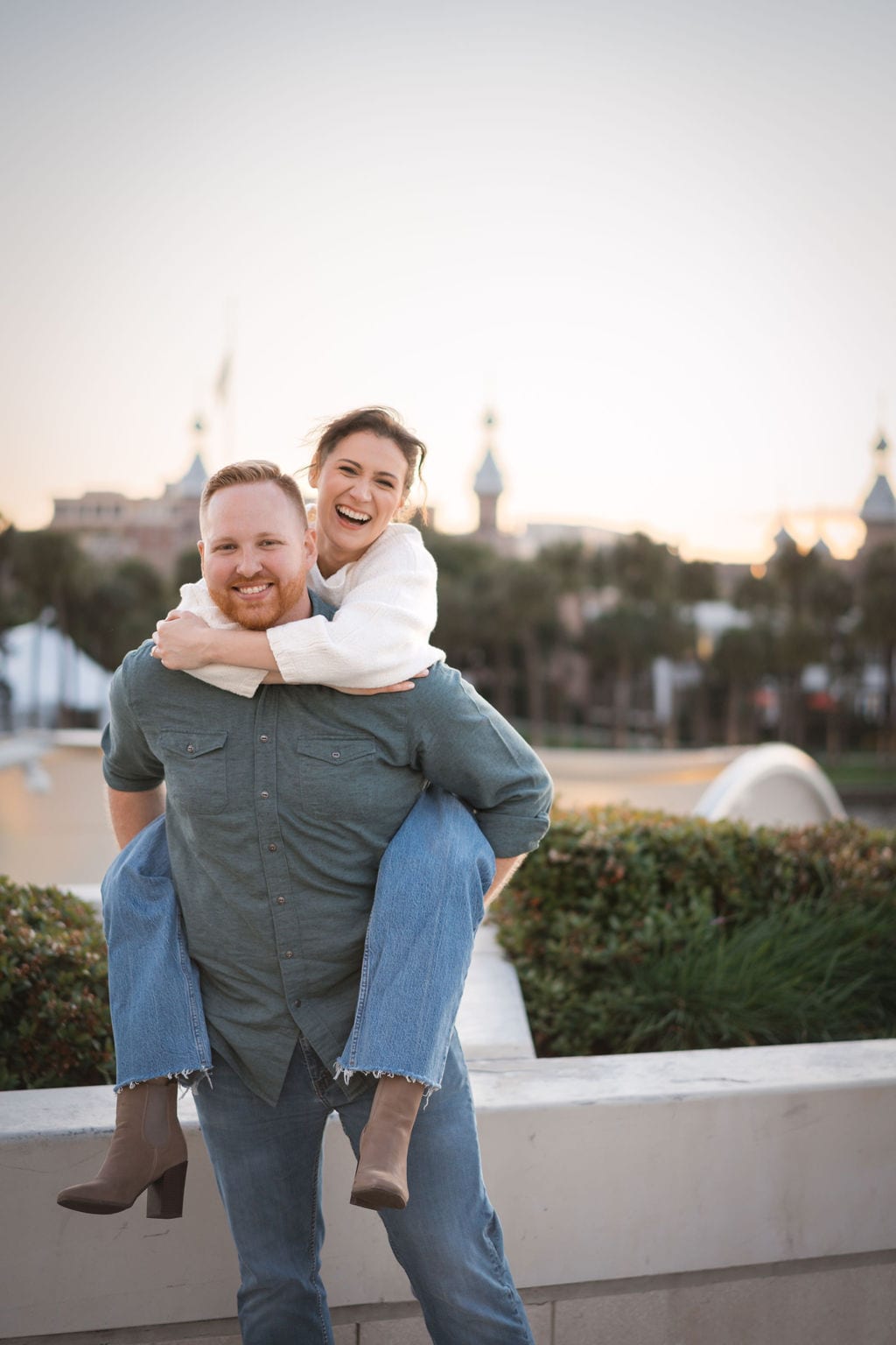 Couple piggyback laughing with University of Tampa minarets behind them