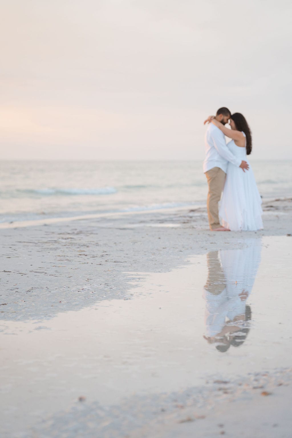 Engaged couple embracing with their reflection in wet sand at a pastel sunset near St. Petersburg