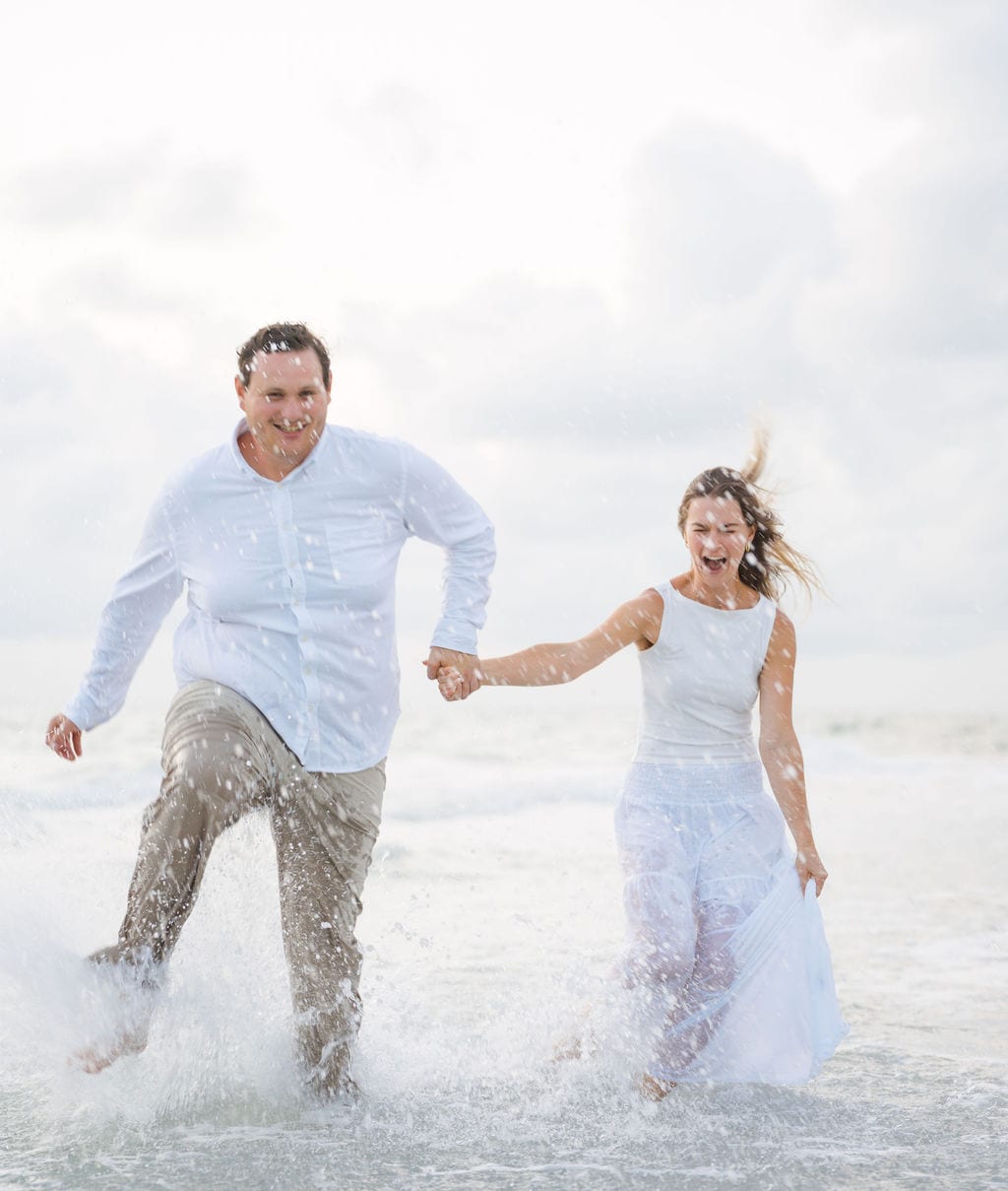Couple running and splashing through waves laughing on a Gulf beach