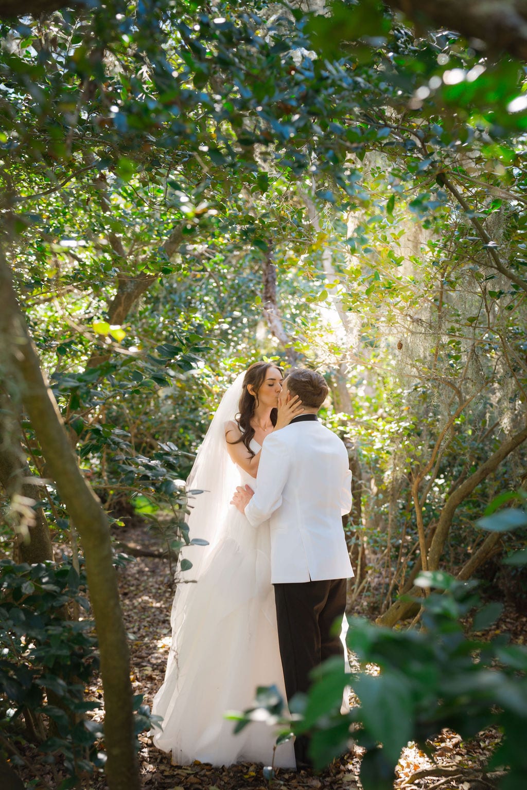 Bride and groom kissing on a wooded path beneath Spanish moss draped oaks