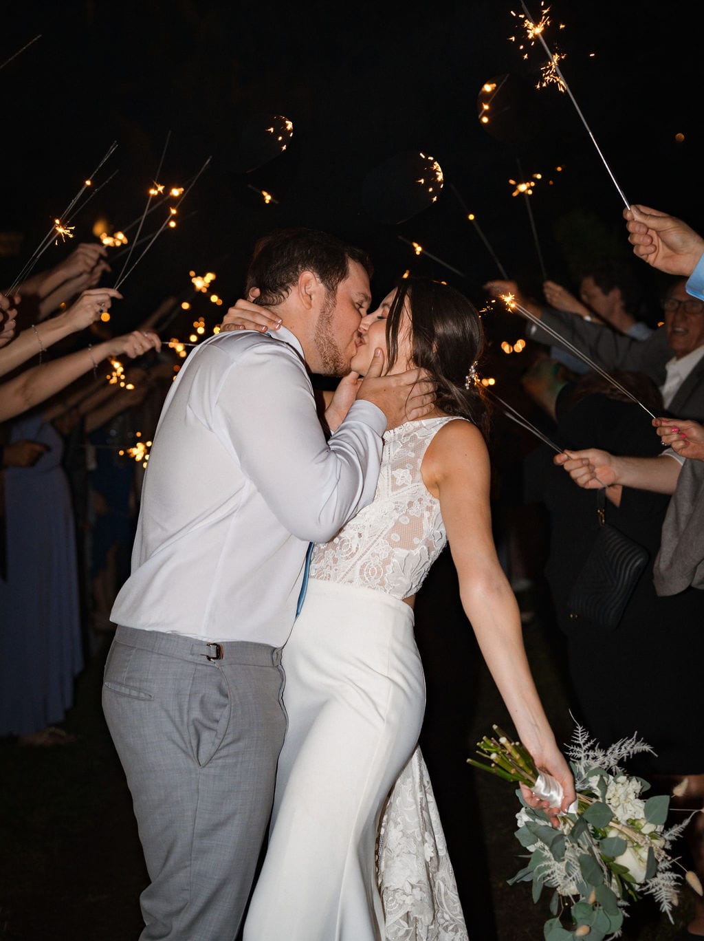 Bride and groom kissing during a sparkler exit at night