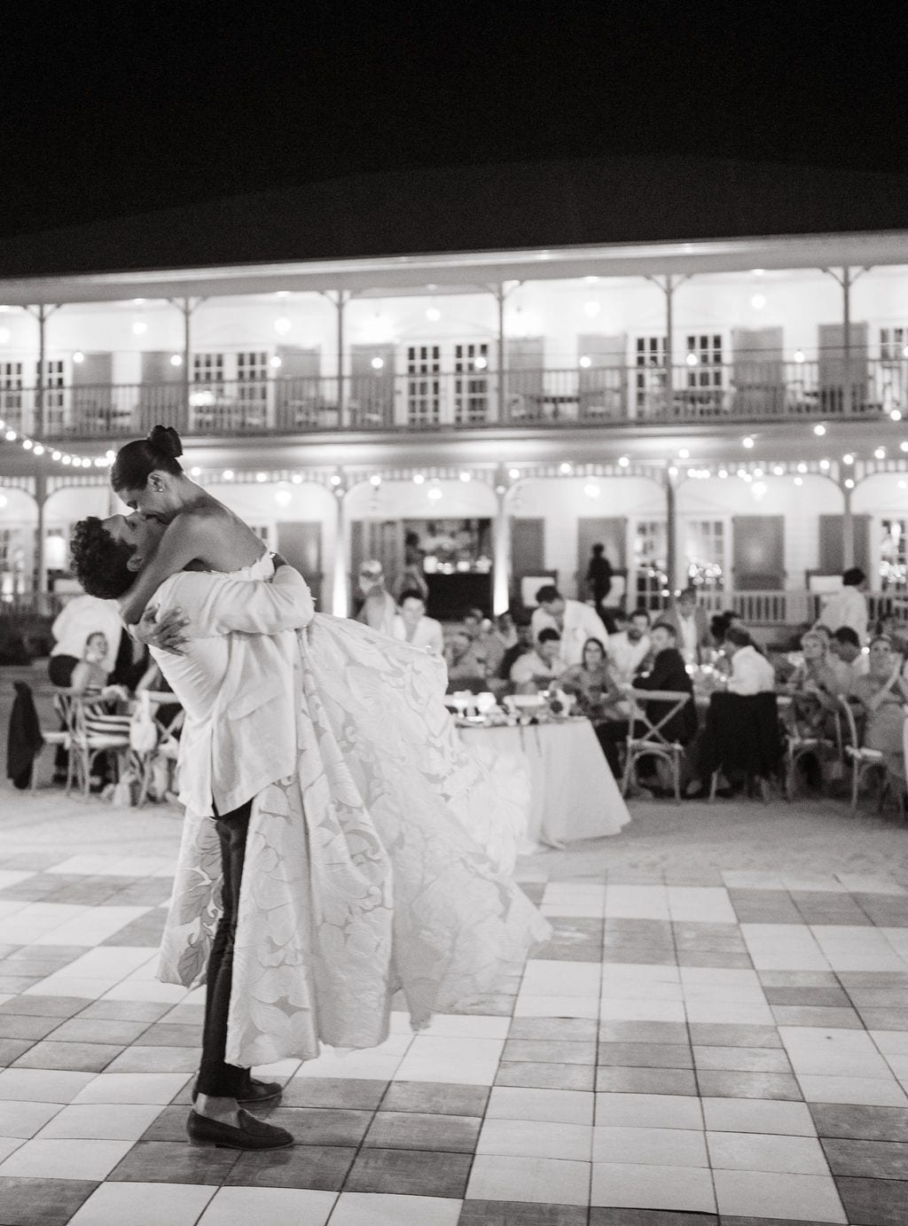 Groom lifting bride during a first dance under string lights at a reception