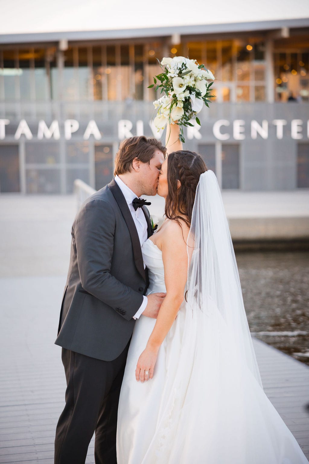 Bride and groom kissing with bouquet raised at a waterfront wedding venue in Tampa