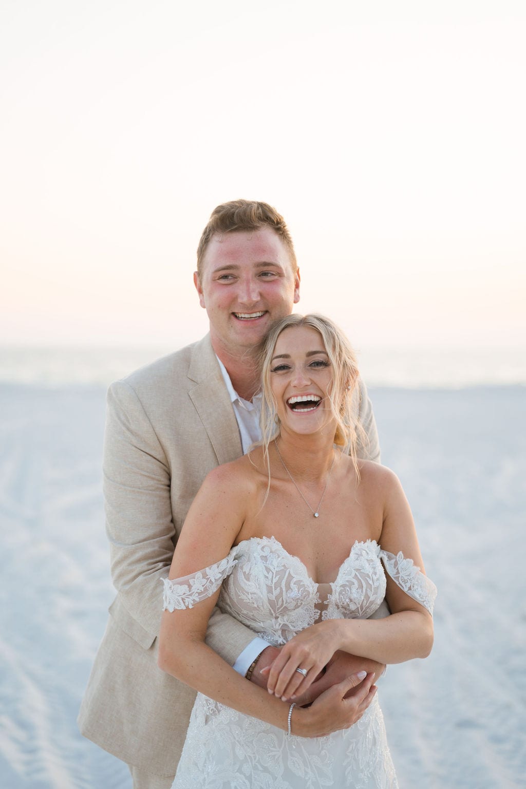 Groom embracing a laughing bride during a beach sunset wedding portrait in Florida
