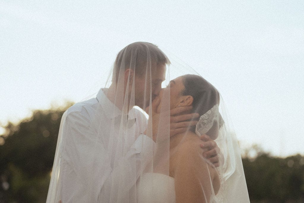 Bride and groom kissing under a veil backlit by a Florida sunset
