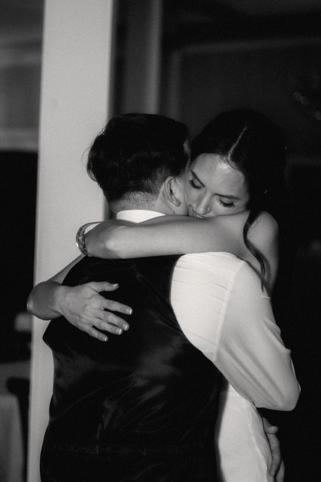 Bride embracing her groom with eyes closed at the reception, black and white